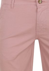 Rosa Baumwollshorts mit einem Reißverschluss und Knopfverschluss, vorderen Taschen und einer glatten Textur mit dezenten Falten.
