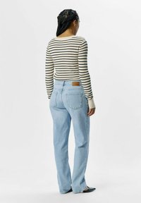 Prugasta majica dugih rukava u krem i mornarskoj boji, u paru sa svijetloplavim trapericama. Traperice imaju stražnje džepove i smeđu oznaku brenda na struku.