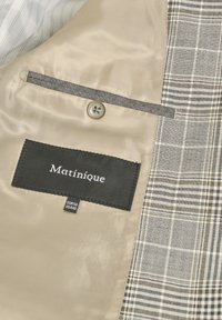Beige lining with a button, featuring a black label reading "Matinique." Plaid design in gray and cream along one side.