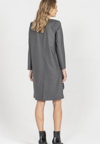 Szara sukienka z mieszanki wełny z długimi rękawami, o prostym kroju i rozcięciu z tyłu. Noszona z czarnymi botkami za kostkę. Gładka faktura i minimalistyczny design.