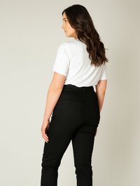 Zwarte high-waisted jeans met achterzakken en een gladde textuur, gecombineerd met een witte top met korte mouwen, gezien van achteren.
