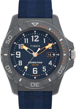 Timex Expedition Solar sat sadrži sivo plastično kućište, plavi teksturirani tekstilni remen, tamnoplavu dial sa valovitim uzorkom i luminescentne kazaljke.