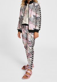 Rosa und schwarze Trainingsanzug mit abstraktem Wellenmuster, zip-feste Jacke, elastische Hosen und rosa Sandalen mit verstellbaren Riemen.