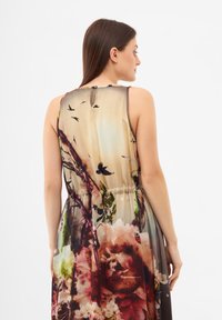Pestrobarevné květinové šaty s gradientním designem a ptáky, elastickým pasem a bezrukávovým střihem, vyrobené z lehkého materiálu.