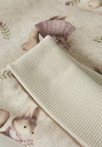 Tessuto di cotone con un motivo di coniglietti e accenti floreali in un delicato beige e in purpurei attenuati, con un bordo finemente ribattuto di crema.