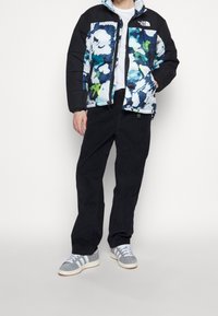 Chaqueta acolchada con un patrón floral en azul, blanco y verde, combinada con pantalones negros y zapatillas grises con rayas blancas.