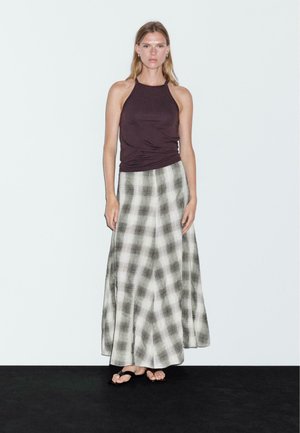 Haut en halter noir associé à une longue jupe à carreaux dans des tons clairs et foncés, avec un design fluide et une texture de tissu douce.