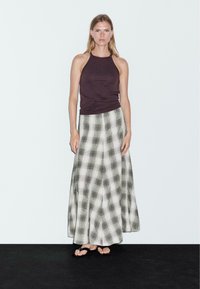 Top a fascia viola scuro con una lunga gonna a quadretti nei toni grigi e bianchi, realizzata in tessuto leggero e dal design fluido.