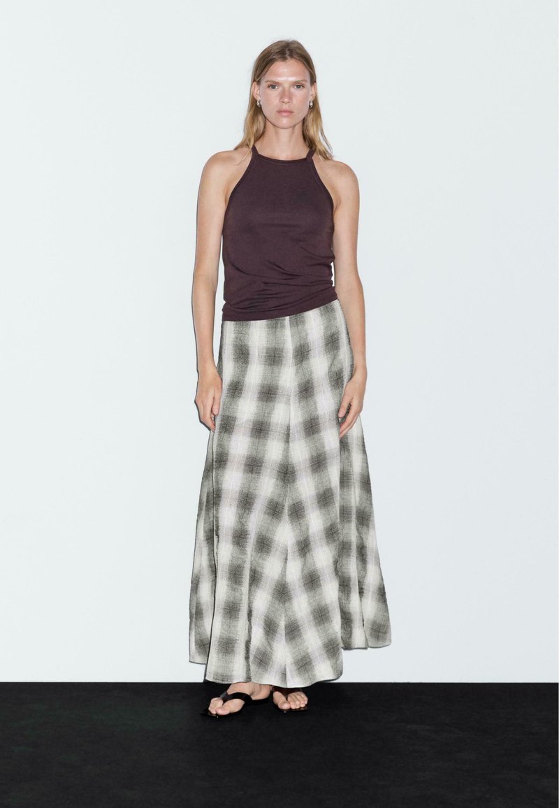 Top a fascia viola scuro con una lunga gonna a quadretti nei toni grigi e bianchi, realizzata in tessuto leggero e dal design fluido.