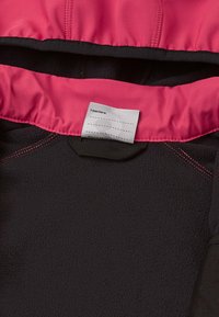Veste en polaire noire avec une doublure intérieure rose. Présente des coutures roses contrastantes et une étiquette portant la mention "J'étais ici :" à l'intérieur du col.