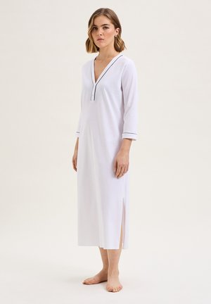 Camicia da notte bianca con scollatura a V e maniche a tre quarti, caratterizzata da dettagli in piping nero e spacchi laterali per facilitare i movimenti.