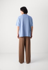 Tricou scurt cu mâneci, de culoare albastru deschis, cu o croială relaxată și o mică imprimare neagră pe partea de jos, asortat cu pantaloni largi de culoare maro.
