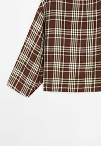 Chemise à carreaux marron et blanche à manches longues et coupe ample, vue de dos sur fond blanc.