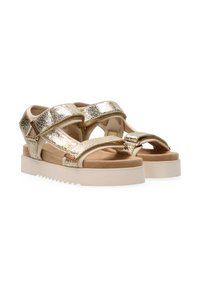 Metall gouden sandalen hebben meerdere banden, een gevoerd voetbed en een dikke, witte plateauzool met een getande rand.