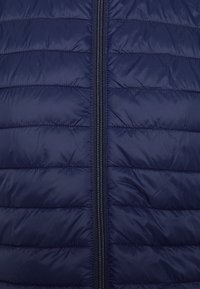 Marineblaues Steppweste mit horizontaler Steppnaht, Frontreißverschluss und glatter, glänzender Textur. Leichtes und isoliertes Design.