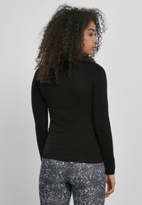 Fekete, hosszú ujjú felső, testhez simuló fazonban, bordás szegéllyel, mintás leggings-szel párosítva, amely szürke és fehér árnyalatokat tartalmaz.