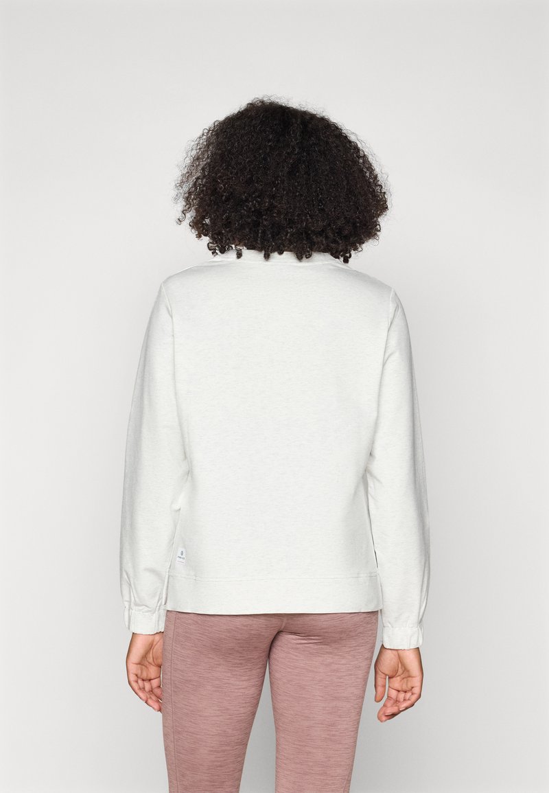 Weißes Sweatshirt mit langen Ärmeln, rundem Ausschnitt und gerippten Bündchen, kombiniert mit rosafarbenen, enganliegenden Leggings, von hinten betrachtet.