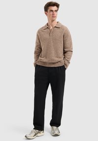 Beige gebreide pullover met een kraag en een knoop, gecombineerd met losse zwarte broeken en zilveren sportschoenen.
