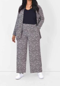 Černobíle vzorovaný outfit zahrnující dlouhý rukáv s bundou a široké kalhoty, doplněný námořnickou halenkou a bílými teniskami.