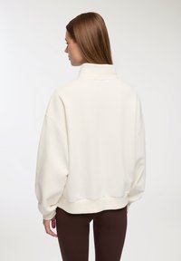 Kremowa, oversize'owa bluza z wysokim kołnierzem, opadającymi ramionami i ściągaczem na dole. Miękka tkanina o gładkiej fakturze.