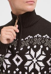Dunkelbrauner Zip-Pullover mit hohem Rippenkragen, der weiße und graue Schneeflockenmuster aufweist und einen Lederreißverschluss mit dem Etikett "isolid" hat.