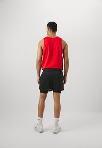 Top sin mangas rojo combinado con pantalones cortos de malla negros. Calcetines blancos y zapatillas deportivas completan el look. Diseño simple sin patrones.