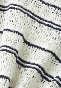 Couverture tricotée avec une base blanche et des rayures bleu marine. La texture est ajourée avec des motifs ouverts, créant une apparence légère et aérée.