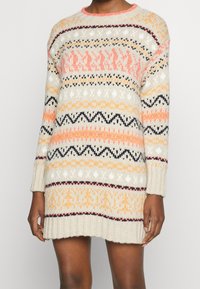 Abito maglione a maglia di colore crema con motivi multicolori. Presenta maniche lunghe, scollo rotondo e bordi a costine. I colori includono rosa, arancione e nero.