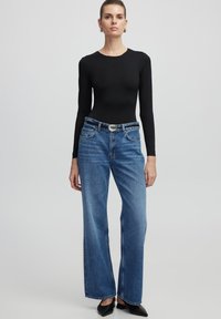 Zwart langarm bodysuit gecombineerd met lichtblauwe wijde jeans, voorzien van een zilveren gespsluiting en puntige zwarte schoenen.