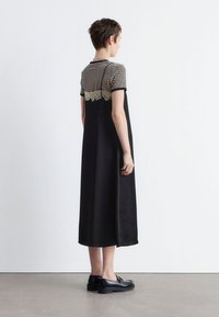 Schwarzes Maxikleid mit einem gestreiften Kurzarmoberteil, das eine Spitzenakzentuierung am Rücken hat, und schwarzen Schuhen mit einer dicken Sohle.