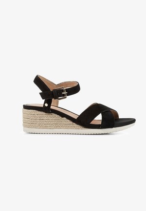 Sandales à talons compensés en daim noir avec des sangles croisées, boucle de cheville réglable et semelle intermédiaire en jute tressé. Semelle extérieure en caoutchouc plat pour une meilleure adhérence.