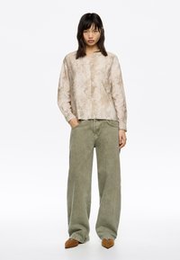 Camisa de botones en color beige claro con estampado de serpiente texturizado, combinada con pantalones de pierna ancha en verde oliva, que cuentan con bolsillos profundos y un ajuste relajado.