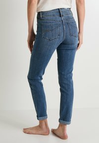Jeans de mezclilla azul con un ajuste slim, cintura de media altura, puños enrollados y bolsillos traseros con un sutil detalle de costura. Textura de tela suave.