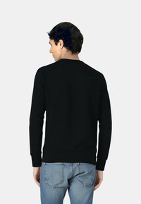 Schwarzer Sweatshirt mit Rundhalsausschnitt und langen Ärmeln, mit gerippten Bündchen und Saum. Trägt dazu eine hellblaue Jeans, von hinten gezeigt.