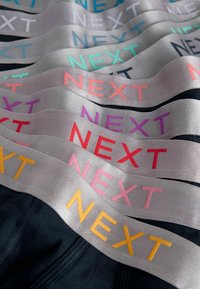 Elastične trake u raznim bojama (roza, narančasta, ljubičasta, plava) s istaknutim natpisom "NEXT". Glatka, satenska tekstura, slojeviti dizajn.