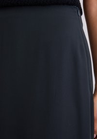 Schwarzer, hoch taillierter Rock aus glattem Stoff, mit einem seitlichen Reißverschluss. Die Textur ist elegant, ohne sichtbare Muster oder Akzente.