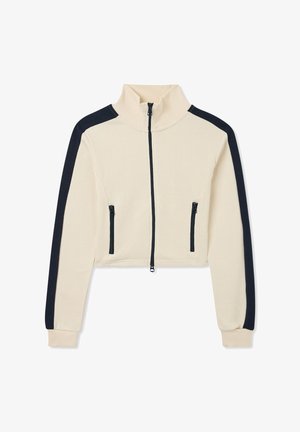 Giacca cropped in tessuto crema con strisce laterali navy. Collo alto, zip anteriore e due tasche con zip. Texture liscia.