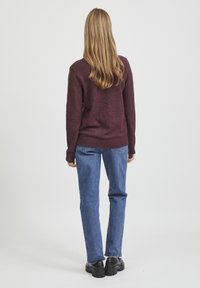 Mörkröd tröja med avslappnad passform och ribbade ärmslut, kombinerad med ljusblå jeans. Svarta klumpiga skor fulländar outfiten.