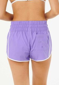 Shorts de bain violets avec taille élastique, bande blanche sur les côtés et une poche arrière avec un détail de logo en relief. Tissu lisse et léger.