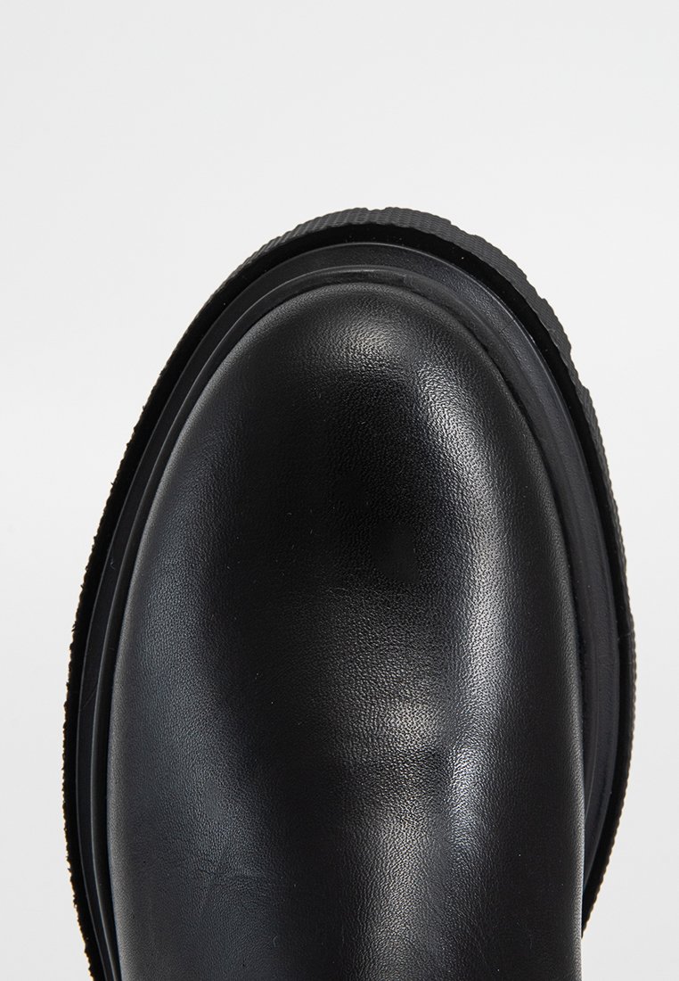 Stivale alla caviglia in pelle nera con punta arrotondata, texture liscia e suola in gomma rigata. Nessun accento o motivo visibile.