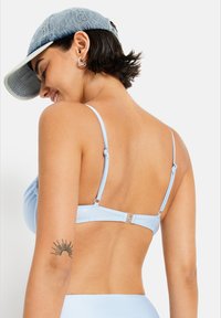 Lyseblå bikini topp med justerbare stropper, rynkede detaljer og en lås bak. Dongerikaps med en litt skrå vinkel.