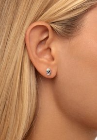 Silberne Totenkopf Ohrringe mit schwarzen Augen und goldenen Akzenten, die über feine Details und eine polierte Oberfläche verfügen, präsentiert am Ohr eines Modells.