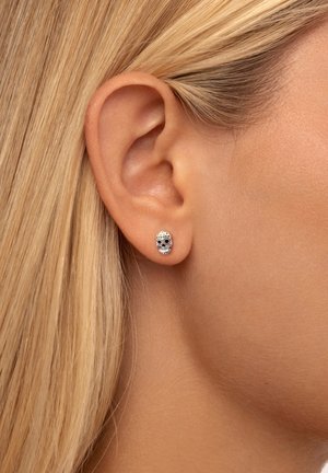 Silver skull earrings with black eyes and gold accents, featuring intricate detailing and a polished finish, displayed on a model's ear.