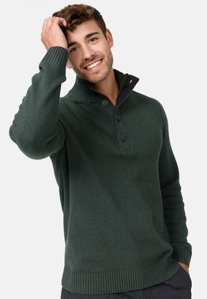 Dunkelgrüner Strickpullover mit hohem Kragen, drei Knöpfen am Hals und gerippten Bündchen und Saum. Glatte Textur mit subtilen Details.