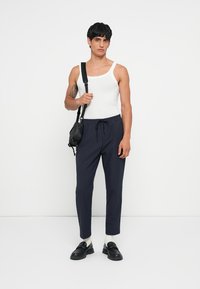 Biela tielko, zúžené námornícke nohavice s šnúrkou; vrstvené s čiernou crossbody taškou a čiernymi mokasínami cez svetlé ponožky. Jednoduchý, moderný dizajn.