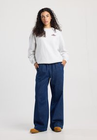 Grijze sweatshirt met ronde hals en geborduurde tekst, gecombineerd met losse donkere spijkerbroek en tan instappers.