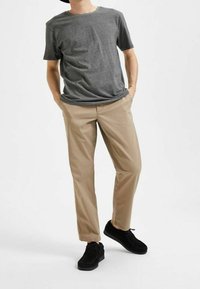 Grå t-shirt med kort ärm i kombination med beige byxor och svarta skor. T-shirten har en slät textur, medan byxorna har en rak passform.