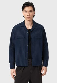 Mørkeblå skjorte med knapper og hvide, lodrette striber, to brystlommer og krave; lavet af let stof med en afslappet pasform.