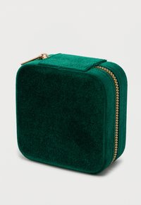 Kompakt, négyzet alakú, zöld velúr ékszerdoboz lekerekített sarkakkal és arany cipzárral, fehér háttér előtt.