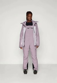 Fialový zateplený lyžařský oblek s odpovídající bundou a laclem, který obsahuje černou kapsu na zip, nastavitelné manžety a elegantní design.